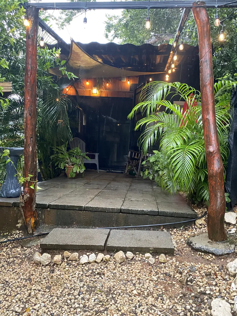 La terrasse couverte du Container Home avec de chaleureuses guirlandes lumineuses, des palmiers en pot et des sièges sous un auvent.
