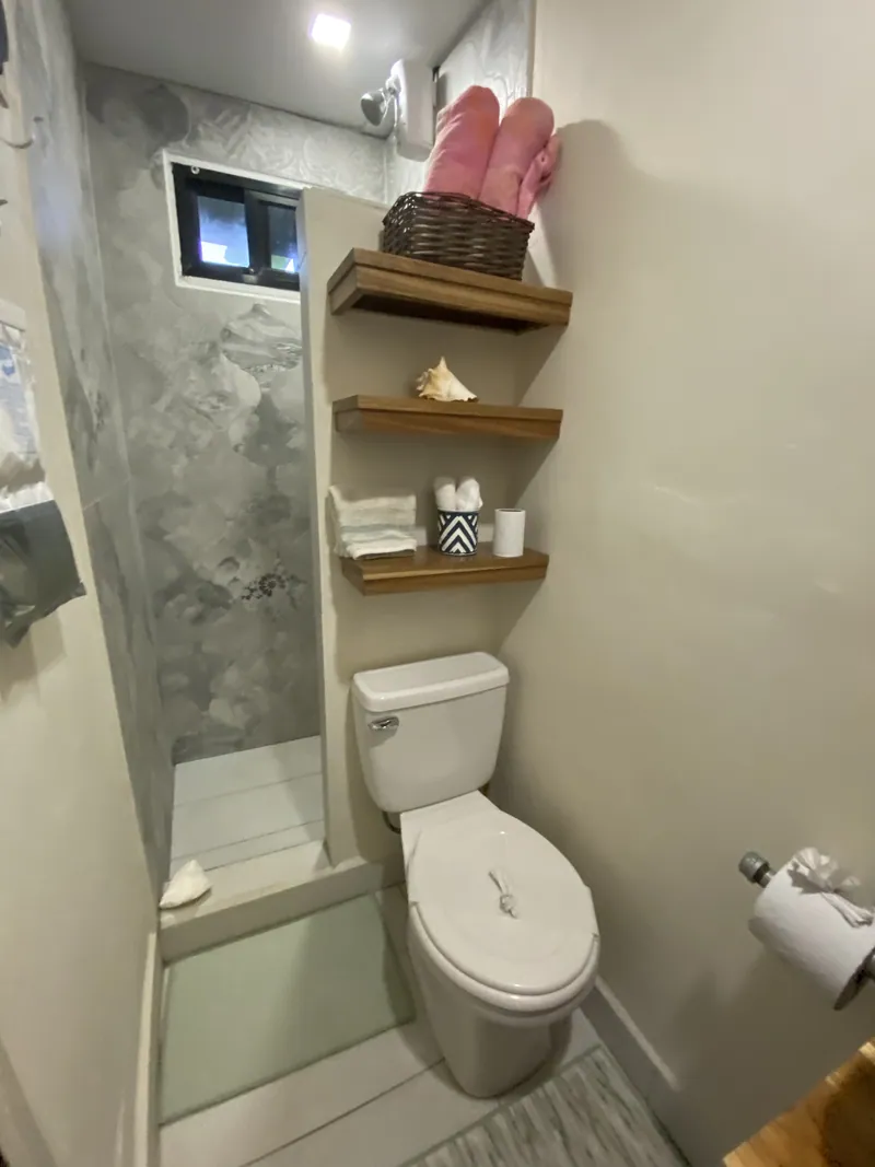 La petite salle de bain avec une douche à l’italienne carrelée, des étagères en bois et des serviettes roulées dans un panier.