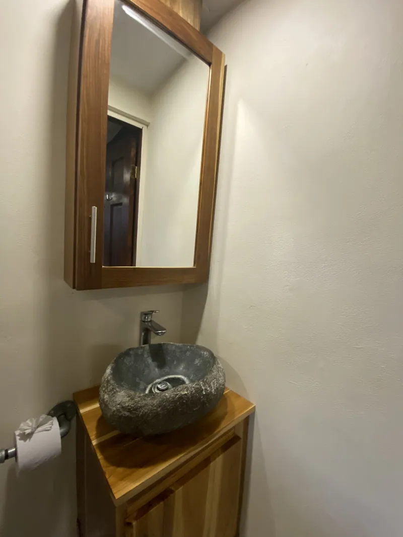 Une vasque en pierre naturelle sur un meuble en bois sous une armoire à miroir encadrée de bois dans la salle de bain.