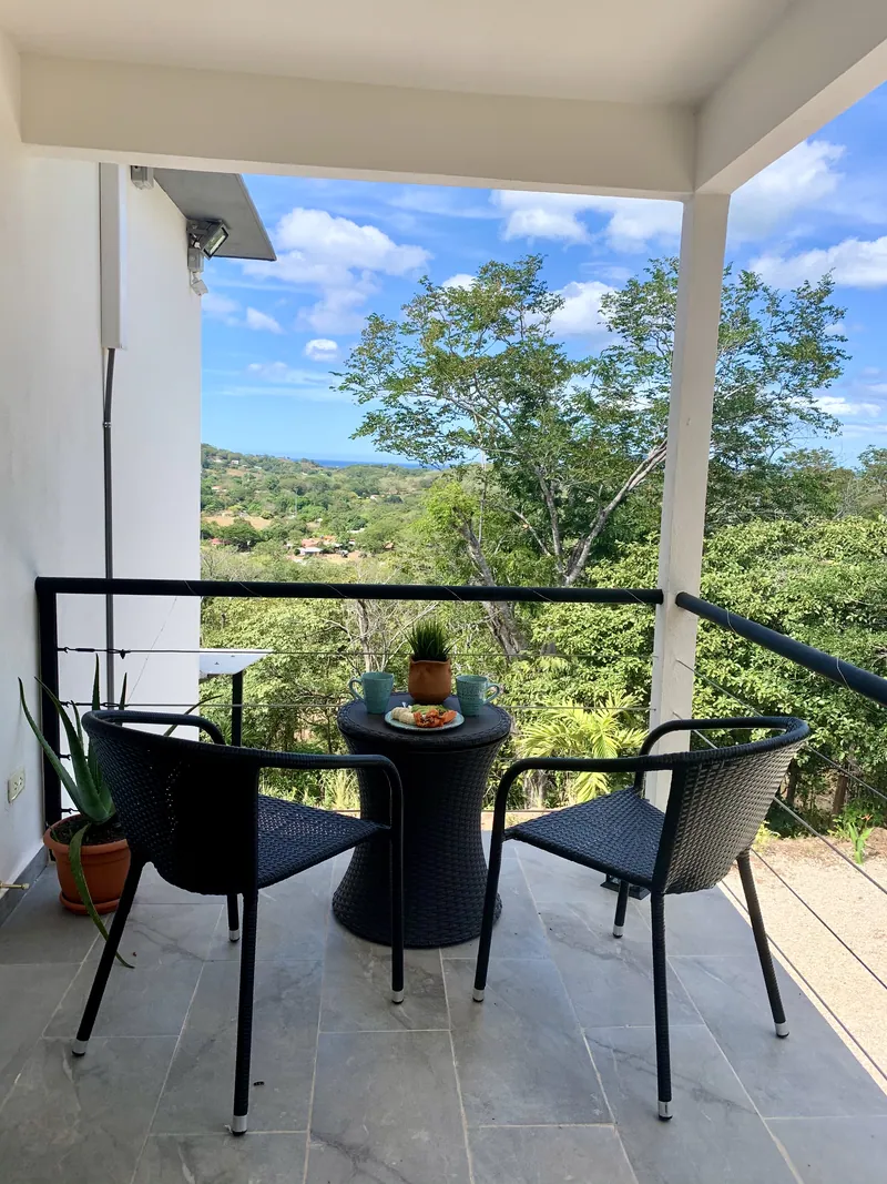 The covered balcony at Villa Alegria, with a bistro table and chairs looking out over the forest to the sea