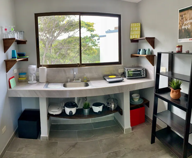 The kitchenette at Villa Alegria, with open shelving, a sink, and a window onto the trees