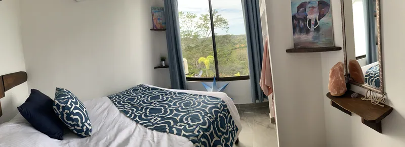 A bedroom at Villa Alegria, the bed dressed in blue beside a window framing the green hills