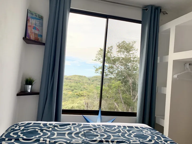 A bedroom at Villa Alegria looking out through a large window over the treetops and valley