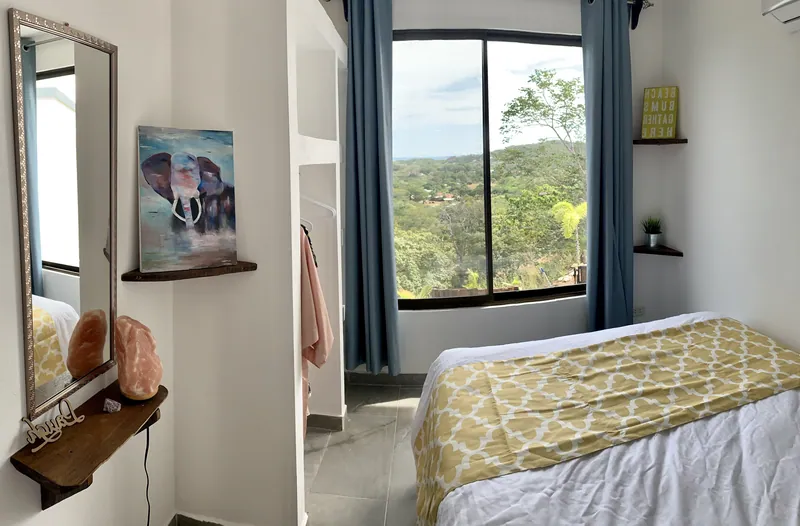 A bedroom at Villa Alegria with a yellow-dressed bed and a window opening onto the forest