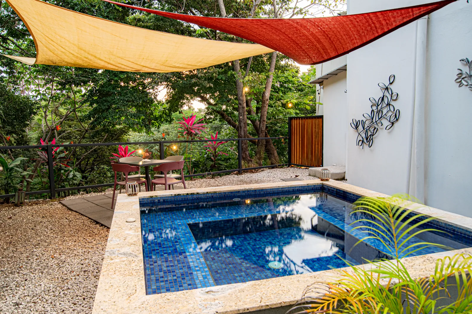 The private plunge pool at Villa Luna, framed by cream and red sun shades and tropical garden