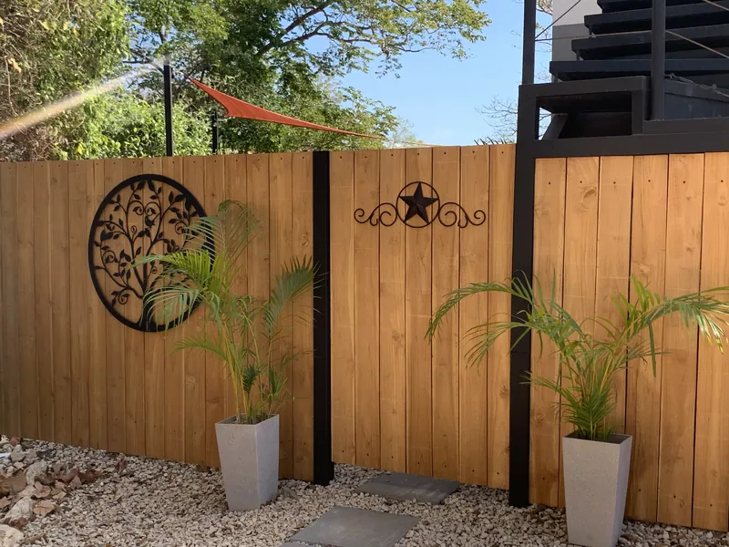 The gravel garden at Villa Luna, teak privacy fencing hung with wrought-iron wall art and flanked by potted palms