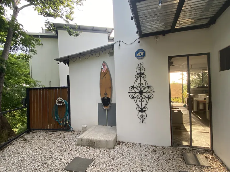 The whitewashed exterior of Villa Luna, a surfboard outdoor shower and sliding glass doors into the living room