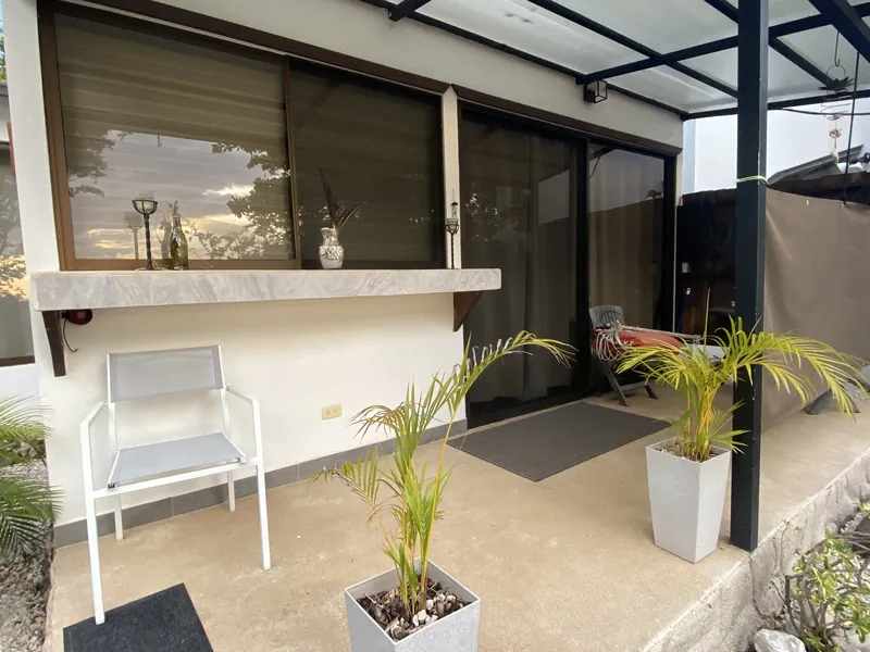 The covered terrace at Villa Luna, a lounge chair and potted palms along a stone bar ledge