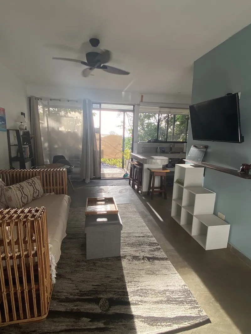 The open living room at Villa Luna, a rattan sofa under a ceiling fan with the kitchen and garden door beyond