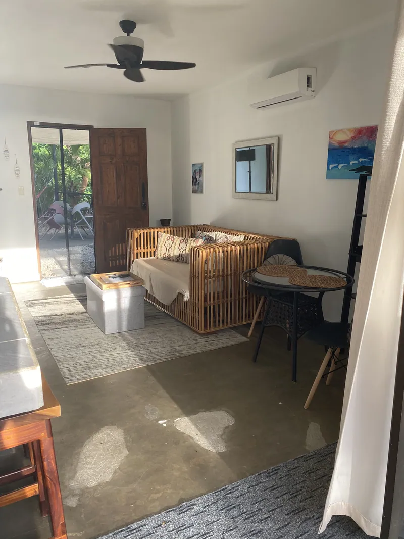 The studio living area at Villa Luna, a rattan daybed and bistro table with the carved wooden door open to the garden