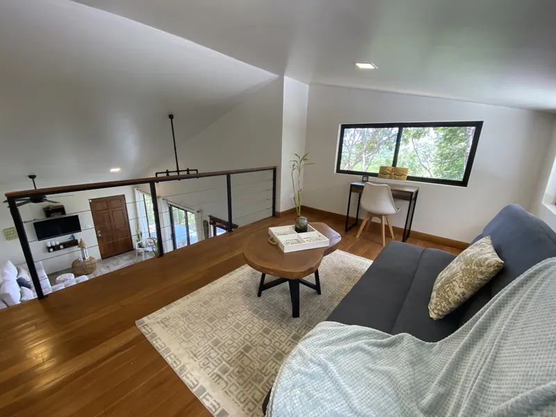 The teak loft lounge at Villa Lunax, a sofa and desk beside a treetop window