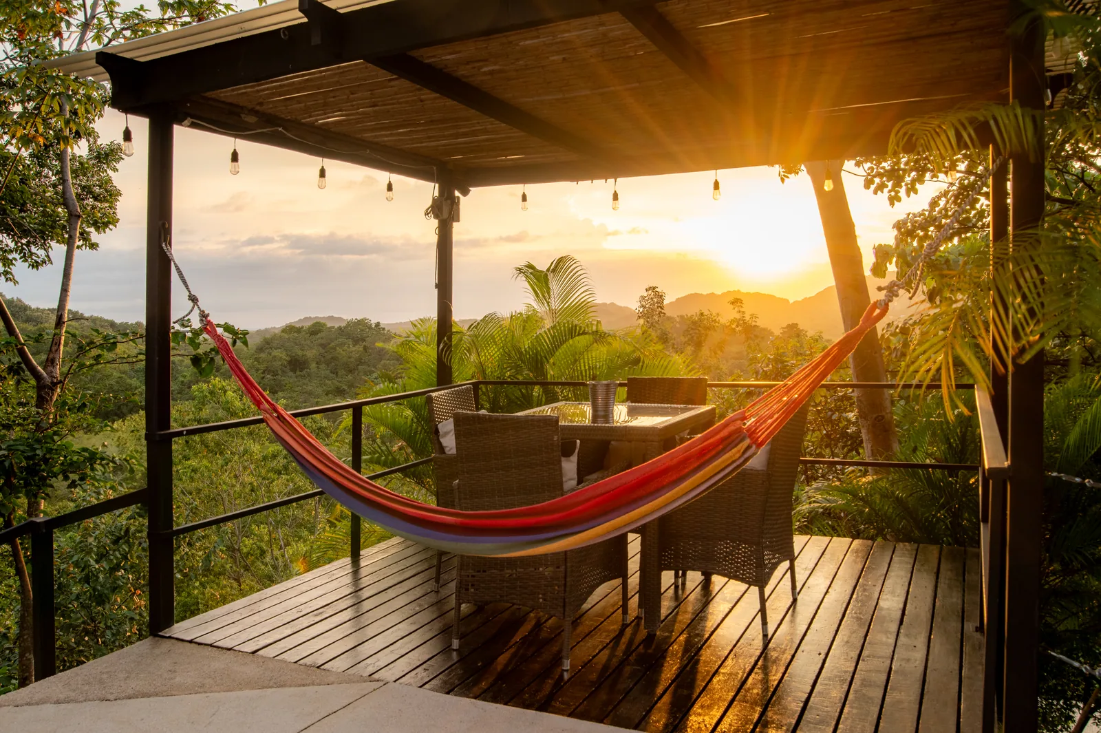 A striped hammock and shaded dining table on the sunset pergola deck at Villa Sol, overlooking the jungle hills