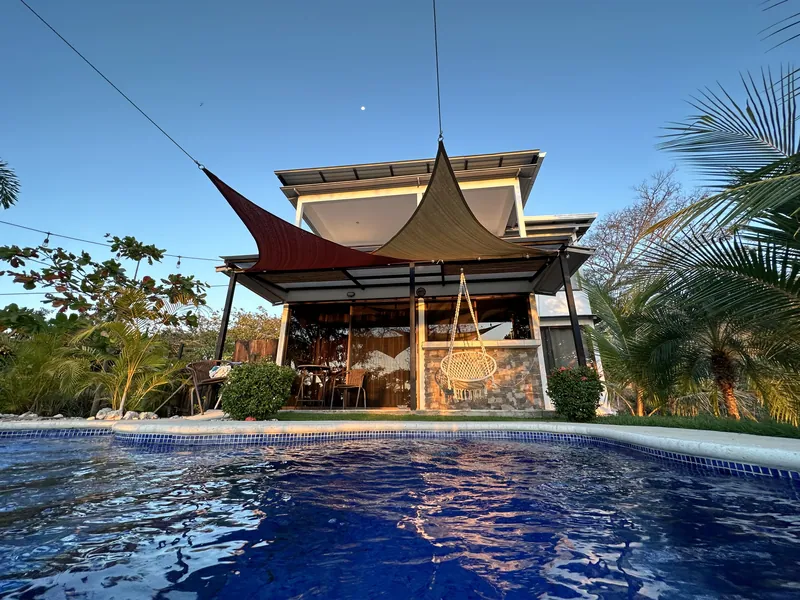 Villa Sol framed by shade sails and palms, mirrored in the pool below
