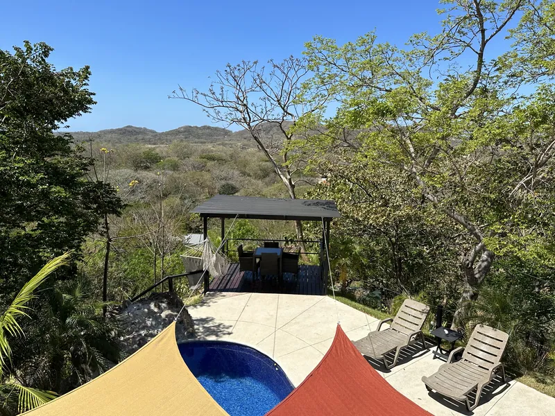 An elevated view over the pool deck, sun loungers and dining gazebo to the hills at Villa Sol