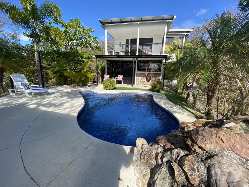 The kidney-shaped pool and Villa Sol with sun loungers and a rock-edged garden