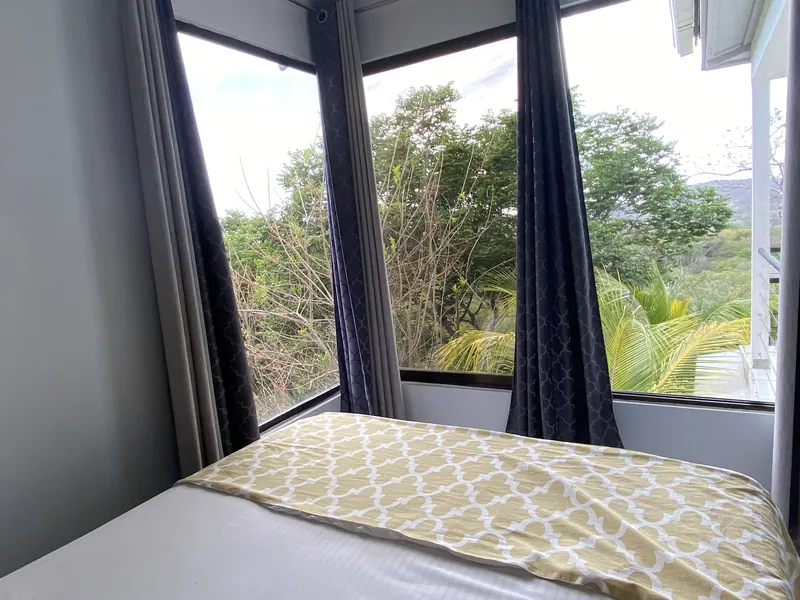 The upstairs bed framed by corner windows onto the jungle at Villa Sol
