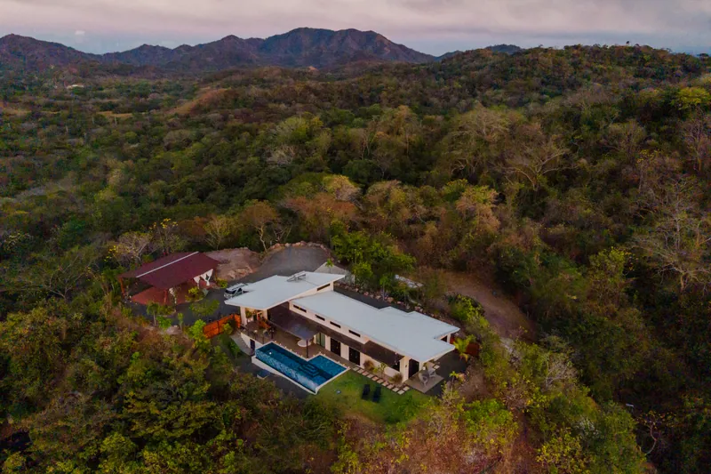 Villa Toltec from above, set into green hillside with mountains on the horizon