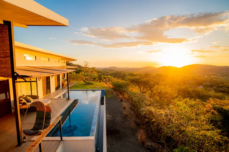 Sunset over the infinity pool and hills, the villa living space alongside