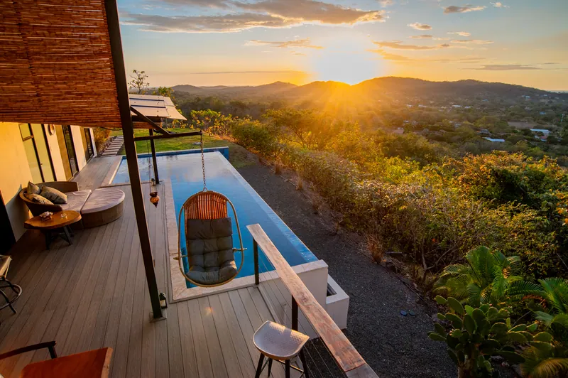 Golden hour on the pool deck, a hanging chair and lounge above the hills
