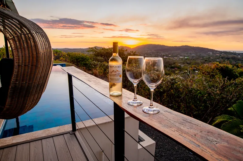 A bottle of wine and two glasses on the deck rail as the sun goes down