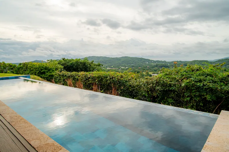 The edge of the infinity pool meeting the green hills on a cloudy day