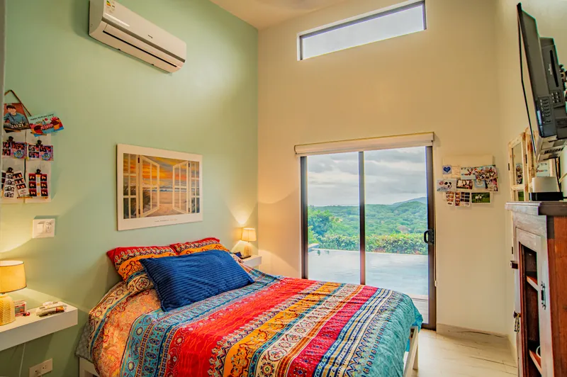 A bright guest bedroom with colourful bedding and sliding doors to the pool view