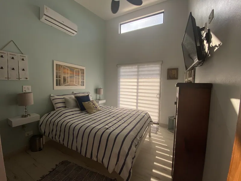 The guest bedroom with striped bedding, a TV and pale wood floors