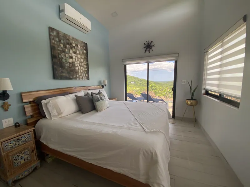 The king bed of the master bedroom under a live-edge headboard, doors to the view