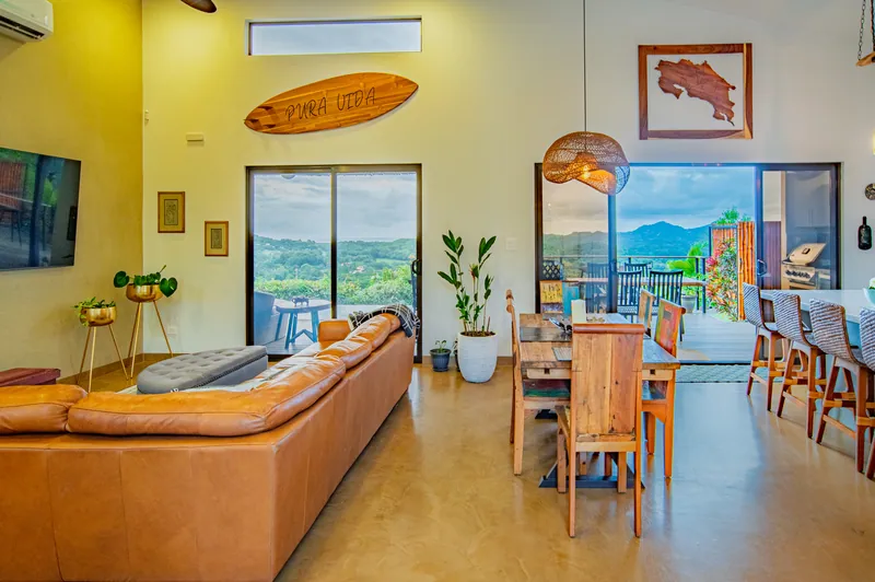 The living and dining space opening to the deck, a Pura Vida surfboard on the wall