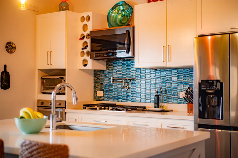 The white kitchen with a blue-tile backsplash, stainless appliances and stone counters